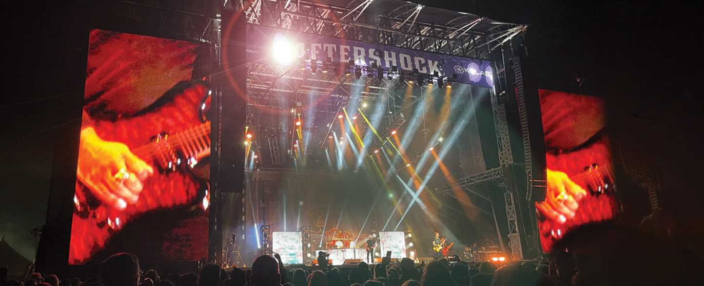 Nighttime concert scene with 'AFTERSHOCK' banner, guitarist